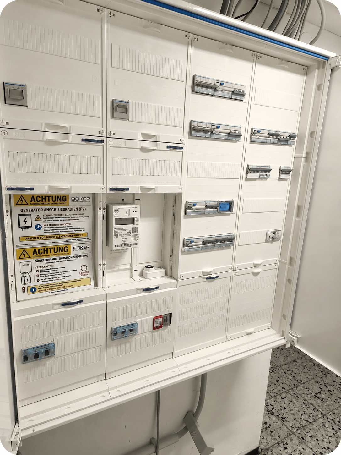 Z&auml;hlerschrank mit Warnschild f&uuml;r anliegende Spannung durch Notstromversorgung aus PV-Hybridwechselrichter auch bei Netztrennung. Der Z&auml;hlerschrank wurde so gebaut zur Versorgung von 2 W&auml;rmepumpen mit W&auml;rmepumpentarif und Haushaltsstrom mit Notstromversorgung bei Stromausfall durch Photovoltaikanlage mit gro&szlig;em Stromspeicher. Auch eine Wallbox , die f&uuml;r bidirektionales Laden zertifiziert ist, wird aus diesem Z&auml;hlerschrank versorgt.